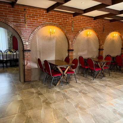 Ceglane łuki, kinkiety i stoliki z czerwonymi krzesłami w części restauracyjnej